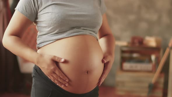 A Pregnant Girl in Jeans and a T-shirt Is Stroking Her Bare Tummy. Hands Stroking a Pregnant Belly