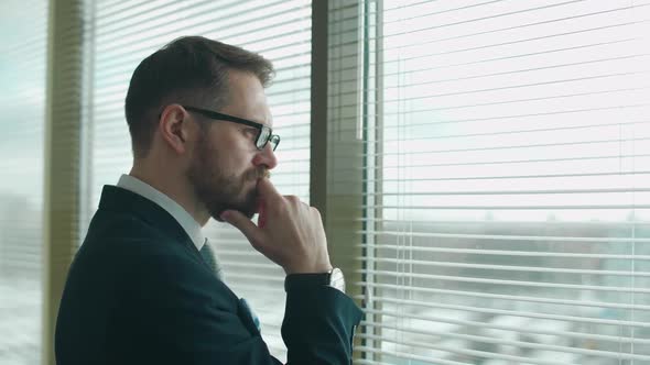 Focused Creative Man in a Suit Stands at the Window in the Office and Reflects the Thinking Process