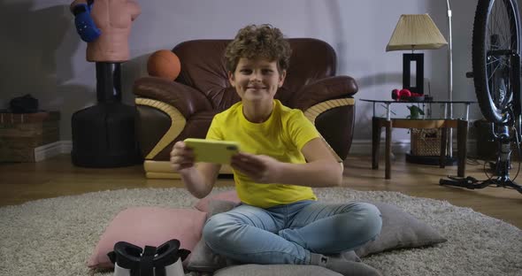 Portrait of Smiling Caucasian Teenager Sitting on the Floor at Home and Playing Video Games. Happy