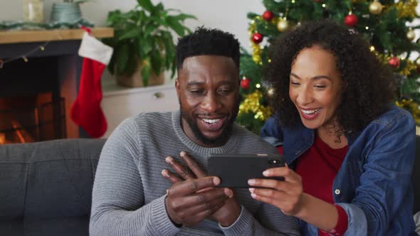 Smiling african american couple having video call and gesturing, christmas decorations in background