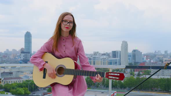 A Young Woman is Playing the Guitar at the Rooftop