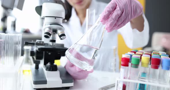 Hand of Scientist Holding Flask with Transparent Liquid in Laboratory Glassware and Test Tubes