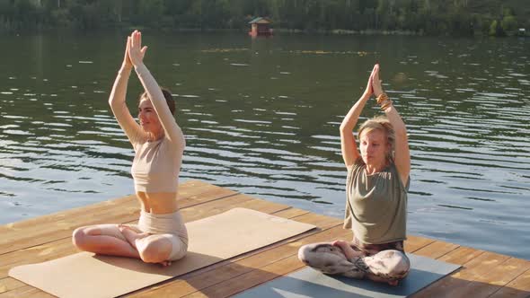 Two Young Ladies Meditating on Lake Pier