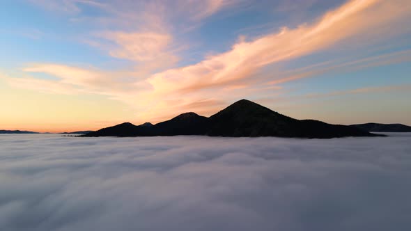 Aerial view of a big mountain over white dense clouds at bright sunrise.