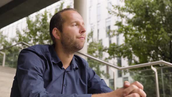 A Caucasian Man Thinks About Something and Nods with a Smile As He Sits on a Staircase