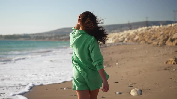 Back View of Slim Cheerful Young Brunette Woman Walking in Slow Motion on Sandy Sunny Beach Turning