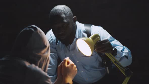 African Officer Interrogating Man Suspected of Crime Glowing Light of Lamp Into Face