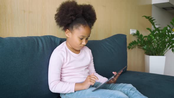 Little Mixedrace Girl Kid Using Digital Tablet Sitting on Couch at Home