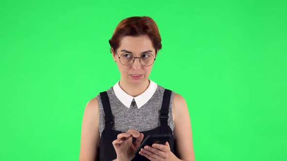 Portrait of Funny Girl in Round Glasses Is Texting on Her Phone and Rejoicing. Green Screen