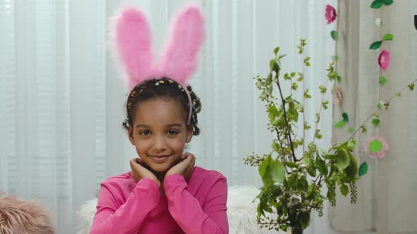 A Cute Little Girl Looks in Funny Pink Bunny Ears Looks at the Camera and Smiles