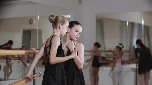 Two Little Girls Whispering Something to Each Other Near the Stand of Ballet Studio