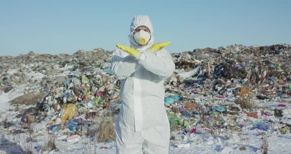 Man in Protective Form Shows Sigh Stop with Crossed Hands Near Landfill