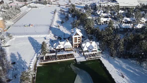 Aerial footage of Zlatibor mountain lake. Snow, ice and trees with people walking by the lake.