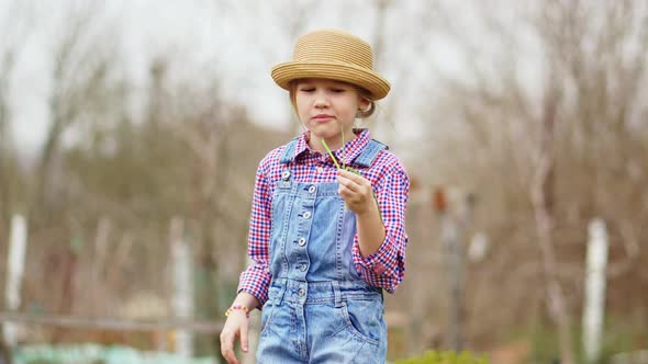 a Funny Little Girl in a Hat Eats Green Onions and Waves at the Sharpness