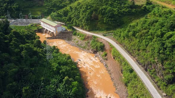 Aerial View of a Hydroelectric Powerplant with Dirty River and Green Forest.