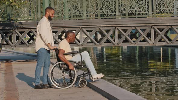 Young Bearded African American Guy Orderly Guardian or Relative Pushing Wheelchair Closer so That