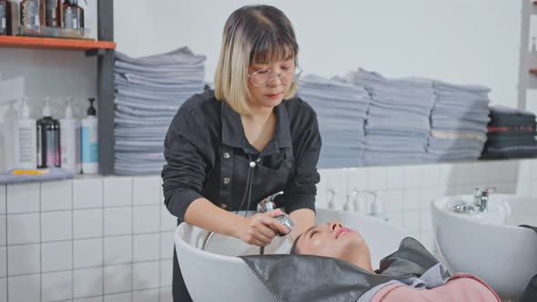 Asian expert Hairdresser massaging and washing hair of young woman in beauty salon or barber.