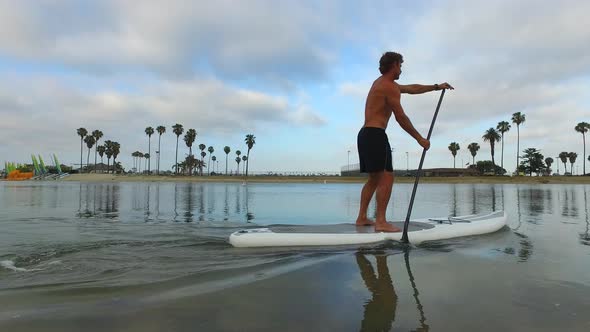 Tracking view of a man paddling his SUP stand-up paddleboard in a lake