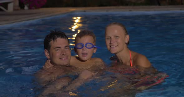 Happy family with child in the pool at night