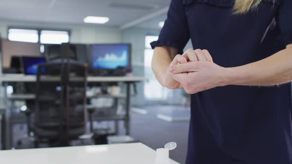 Mid section of woman sanitizing her hands at office