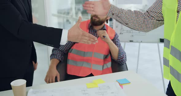 Man in Suit Handshaking with Professional Experienced Engineer in Vest During meeting