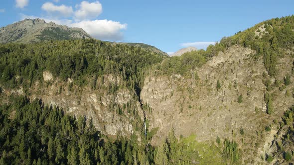 Aerial dolly out over Corbata Blanca thaw waterfall hiding in pine tree woods and mountains, Patagon