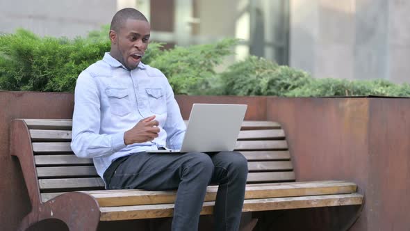 Excited African Man Celebrating Success on Laptop Outdoor