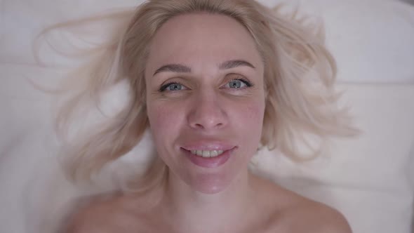 Headshot Portrait of Blond Caucasian Woman with Grey Eyes Looking at Camera Smiling in Slow Motion