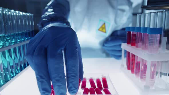 Lab Worker in Protective Uniform Putting Sample Tube with Blood in Container