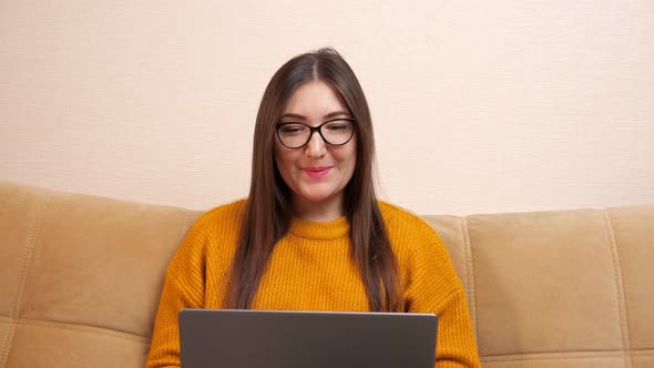 Young Woman Looks on Grey Laptop Display Sitting at Home
