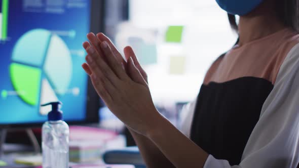 Mid section of asian woman wearing face mask sanitizing her hands at modern office