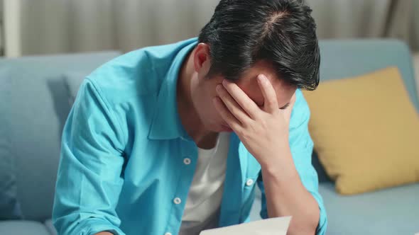 Close Up Of Asian Man With A Laptop Looking At The Bill And Having Headache Due To Financial Problem
