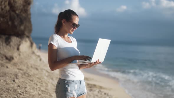 Slender Charming Caucasian Woman in Sunglasses Works with a Laptop