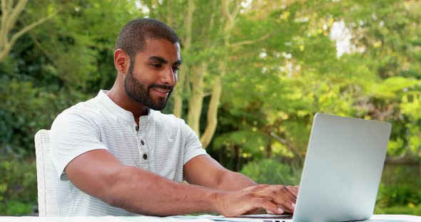 Smiling man using laptop in garden 4k