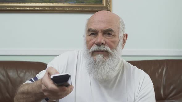 Portrait Mature Senior Man in White T-shirt Sitting on the Brown Leather Sofa Watching TV. Old Man