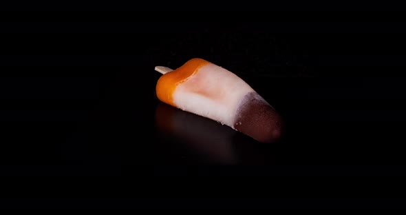 White orange water ice rocket with chocholate top, melts on a black background. Time Lapse.