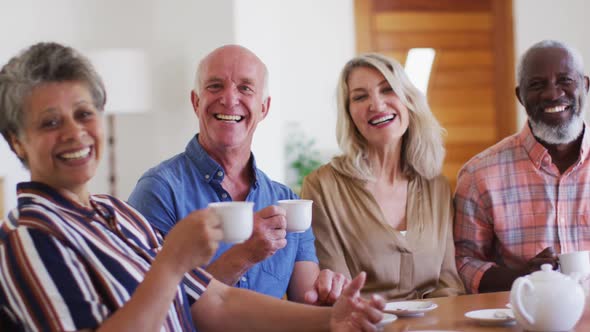 Two diverse senior couples sitting by table drinking tea together at home