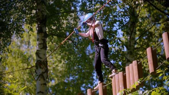 A Woman Carefully Walks on Logs Suspended in the Air Between Trees in the Forest
