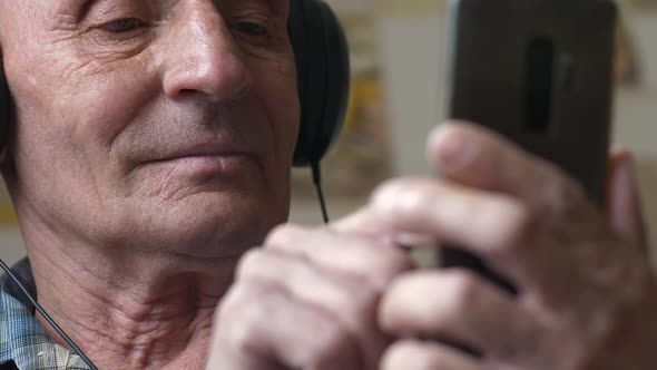 Portrait of a cheerful caucasian pensioner over 70 years old in headphones using a smartphone.pressi