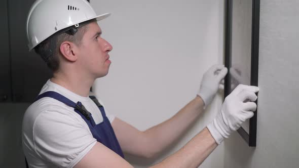 Builder Worker Makes Repairs Hanging Picture or Photo in Frame on Wall