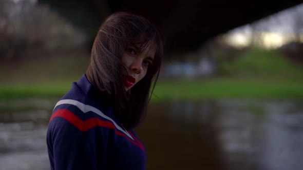 Portrait of a Brunette with Bright Lipstick on Her Lips and in a Blue Jumper on a Cloudy Day. She