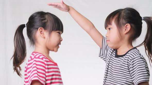 Cute little girl measuring height between herself and her friend with hands on white background