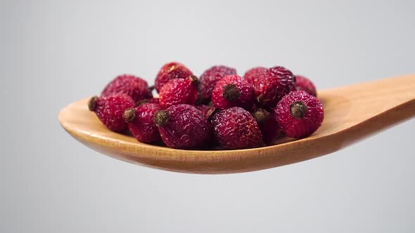 Dried red rosehip berries fall from a wooden spoon on a white background 