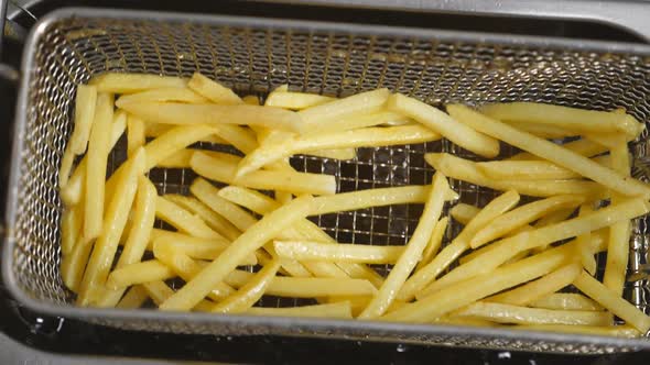 Top View of Male Cook Shaking a Lattice with French Fries Being Prepared in Hot Boiling Oil
