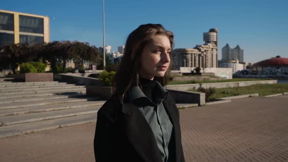 A Serious Brunette Girl Walks Along the Embankment of the Big City