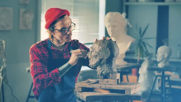 Male Artist is Fixing a Clay Sculpture with a Scraper