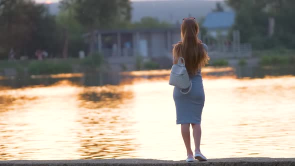 Back View of Lonely Woman Standing on Lake Side on Warm Evening