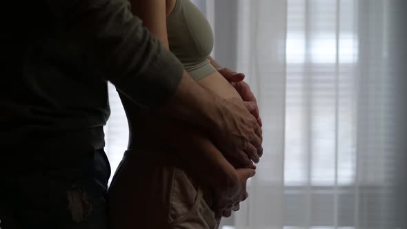 A man walks up to his pregnant wife and strokes her pregnant belly with her