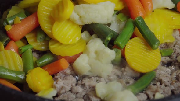 Adding frozen vegetables to minced meat in a pan on stove. Frying minced meat