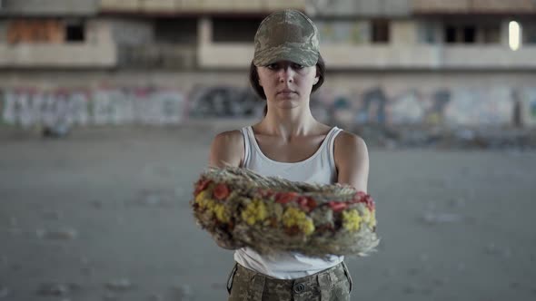 Portrait of a Beautiful Girl in a Camouflage Cap and White T-shirt Holding a Wreath Looking